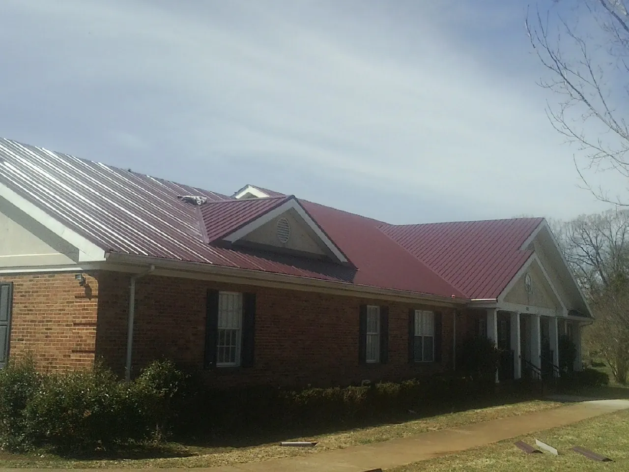 Red metal roof with gabled entries on a long brick building, from a Hail Damage Roof Repair job in Hopedale